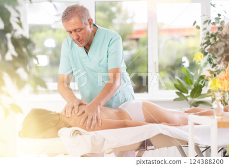 Skilled old masseur conducting back massage for woman client Skilled old masseur conducting back massage for woman client 124388200