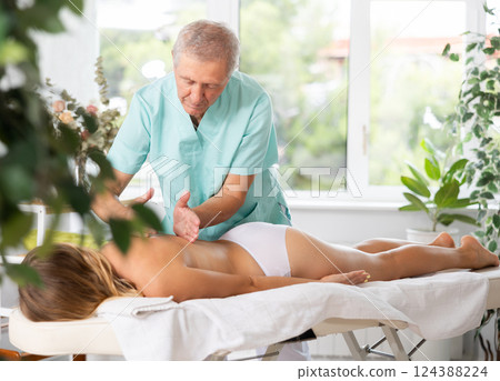 Skilled old masseur conducting back massage for woman client Skilled old masseur conducting back massage for woman client 124388224
