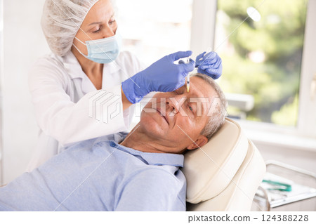 Woman cosmetologist making injections between eyebrows to male patient 124388228