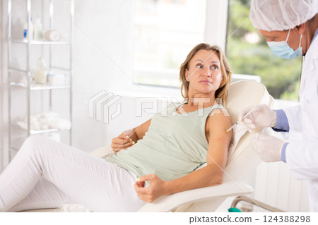 Middle-aged woman having arm injection lying on clinical chair 124388298