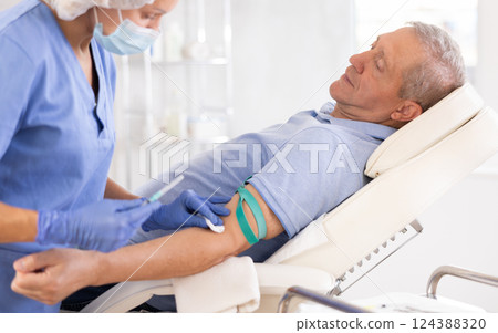 Woman nurse in disposable cap and mask perform procedure of blood drawing for to retired man Woman nurse in disposable cap and mask perform procedure of blood drawing for to retired man 124388320