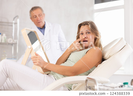 Upset adult woman looking at her face in mirror 124388339