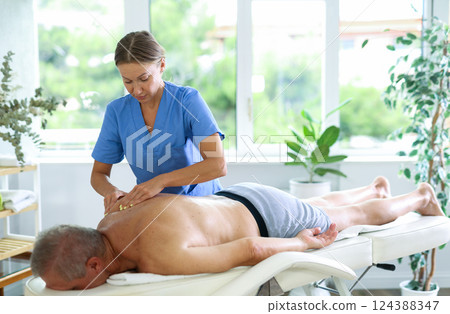 Skilled middle-aged masseuse conducting back massage for man client 124388347