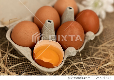 Brown homemade eggs in an egg carton. Broken egg. Raw egg yolk 124391878