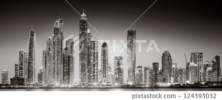 Urban city skyline with illuminated skyscrapers and waterfront railing in black and white at night, Dubai Marina bay UAE 124393032