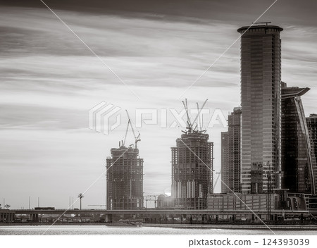 Monochrome city skyline with tall skyscrapers reflecting on calm water under a cloudy sky, Dubai Marina bay UAE Monochrome city skyline with tall skyscrapers reflecting on calm water under a cloudy sky, Dubai Marina bay UAE 124393039
