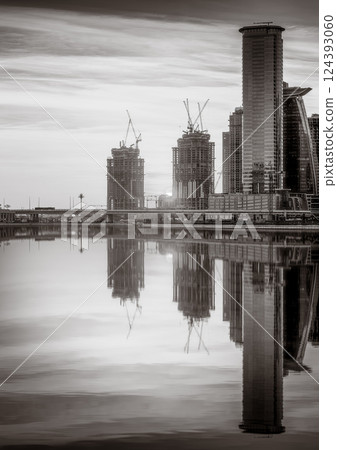 Monochrome city skyline with tall skyscrapers reflecting on calm water under a cloudy sky, Dubai Marina bay UAE Monochrome city skyline with tall skyscrapers reflecting on calm water under a cloudy sky, Dubai Marina bay UAE 124393060