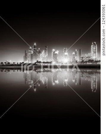 Urban city skyline with illuminated skyscrapers and waterfront railing in black and white at night, Dubai Marina bay UAE 124393061