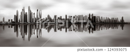 Monochrome city skyline with tall skyscrapers reflecting on calm water under a cloudy sky, Dubai Marina bay UAE Monochrome city skyline with tall skyscrapers reflecting on calm water under a cloudy sky, Dubai Marina bay UAE 124393075