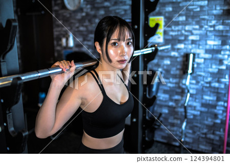 A cool woman working out at the gym, carrying a barbell on a power rack machine, muscle training girl A cool woman working out at the gym, carrying a barbell on a power rack machine, muscle training girl 124394801