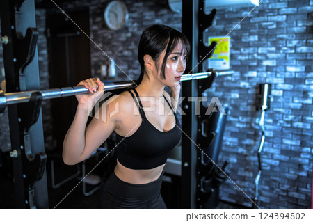 A cool woman working out at the gym, carrying a barbell on a power rack machine, muscle training girl A cool woman working out at the gym, carrying a barbell on a power rack machine, muscle training girl 124394802