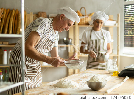Elderly man and woman sift flour and whipping dough Elderly man and woman sift flour and whipping dough 124395038