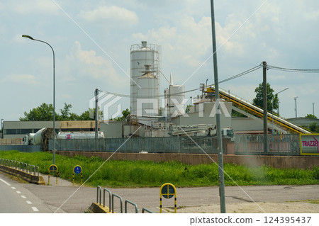 Manufacturing facility with towering silos and conveyor belts under a bright sky in a bustling industrial area Manufacturing facility with towering silos and conveyor belts under a bright sky in a bustling industrial area 124395437