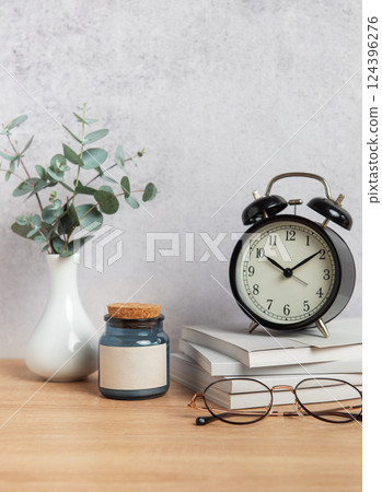 Alarm clock, books, eyeglasses, candle and eucalyptus branches on wooden desk 124396276