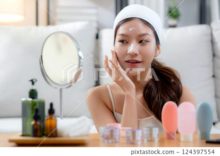 Beauty young asian woman applying cream on facial for wrinkles while looking mirror in living room. Beauty young asian woman applying cream on facial for wrinkles while looking mirror in living room. 124397554