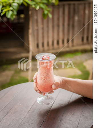 Top view of hand holding a strawberry milkshake on table, Hands showing strawberry smoothie on wooden table. Hands holding strawberry smoothie on wooden table with blurred background Top view of hand holding a strawberry milkshake on table, Hands showing strawberry smoothie on wooden table. Hands holding strawberry smoothie on wooden table with blurred background 124399415