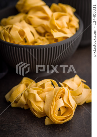 Italian pasta tagliatelle. Uncooked noodle pasta on black table. 124400331