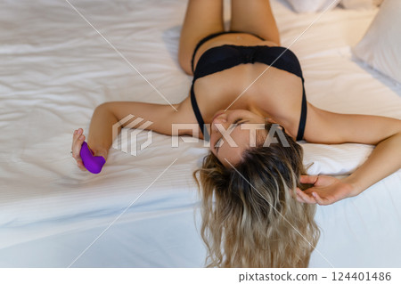 Woman in bed under sheets holding vibrator in hand Woman in bed under sheets holding vibrator in hand 124401486