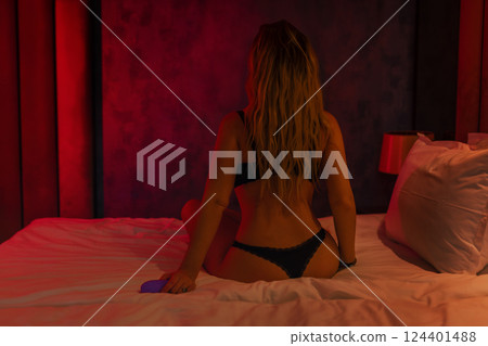 Woman in bed under sheets holding vibrator in hand 124401488