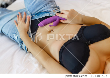 Woman in bed under sheets holding vibrator in hand 124401504