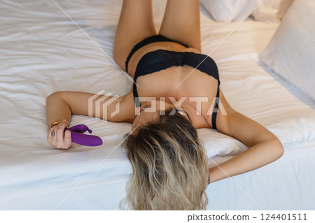 Woman in bed under sheets holding vibrator in hand 124401511