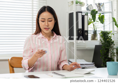 Home Office and Focused Work. A woman analyzing data on her smartphone in her workspace. 124401526