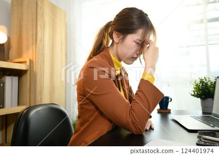 Exhausted young businesswoman sitting at office desk suffering from headache 124401974