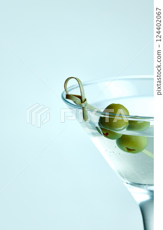 Minimalist close-up of Martini with olives on light background. cocktail garnished with green olives in classic Martini on icy blue background. 124402067