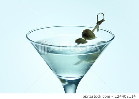 Dry Martini cocktail with green olives on icy blue background. Cocktail with cold vermouth and olives served in classic glass. Dry Martini cocktail with green olives on icy blue background. Cocktail with cold vermouth and olives served in classic glass. 124402114