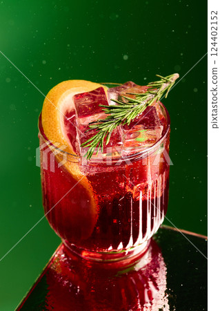 Garnished red cocktail on green background. Classic Negroni cocktail with rosemary and citrus, served in elegant glass over green surface. 124402152