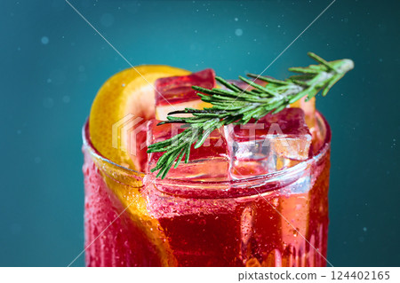 Close-up of cocktail with rosemary and grapefruit on teal background. Refreshing cocktail topped with ice cubes, garnished with rosemary and citrus. Close-up of cocktail with rosemary and grapefruit on teal background. Refreshing cocktail topped with ice cubes, garnished with rosemary and citrus. 124402165