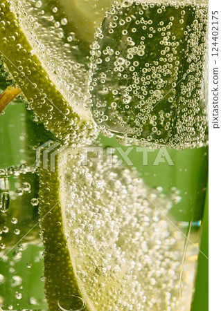 Macro shot of fizzy lime slice and ice cube in cocktail glass full of bubbles. Concept of refreshing drinks. Ad Macro shot of fizzy lime slice and ice cube in cocktail glass full of bubbles. Concept of refreshing drinks. Ad 124402175
