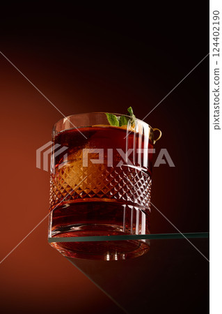 Tumbler glass with whiskey and citrus peel on dark orange background glowing with warmth. 124402190