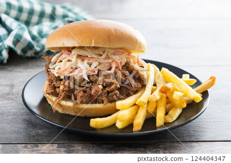 Pulled pork sandwich with coleslaw salad and french fries on wooen table 124404347
