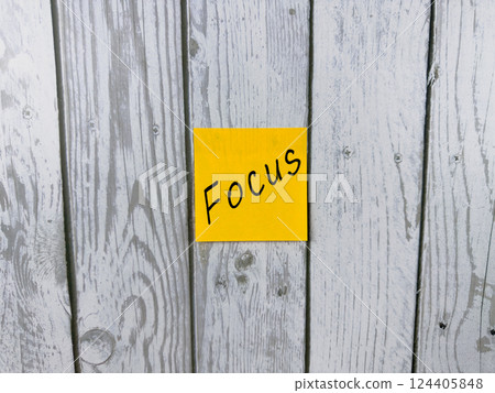 Sticky note with the word Focus written on it, placed on a rustic wooden background. Perfect for concepts of concentration, achieving goals, and staying determined in tasks Sticky note with the word Focus written on it, placed on a rustic wooden background. Perfect for concepts of concentration, achieving goals, and staying determined in tasks 124405848