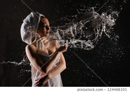 Woman in towel playing with water droplets in a creative indoor setting 124406101