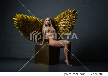 Ethereal figure with golden wings posing elegantly on a pedestal indoors Ethereal figure with golden wings posing elegantly on a pedestal indoors 124407016