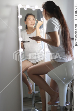 Young asian woman applying makeup in front of mirror with lights 124407219