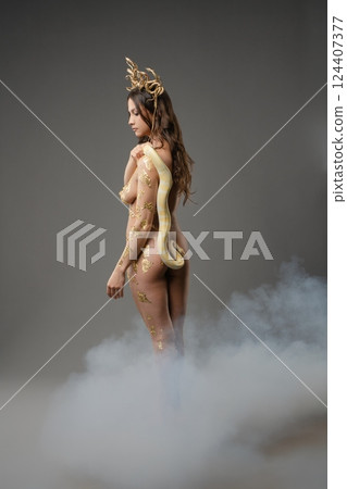 Elegant woman poses gracefully in artistic nude with serpent and gold accents 124407377