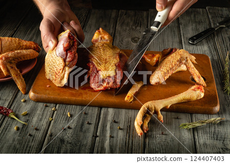 Hands expertly cut through raw poultry, showcasing various parts on a wooden cutting board, in a warm, rustic kitchen setting with dried herbs nearby Hands expertly cut through raw poultry, showcasing various parts on a wooden cutting board, in a warm, rustic kitchen setting with dried herbs nearby 124407403