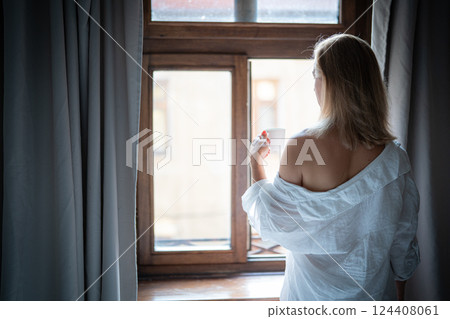 Woman in elegant robe drinking coffee in hotel room and standing near window 124408061