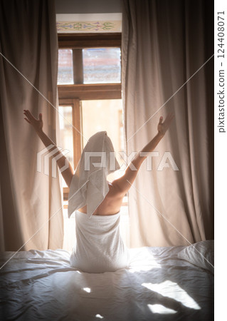 Back view of young woman in towel sitting on bed and meditating Back view of young woman in towel sitting on bed and meditating 124408071