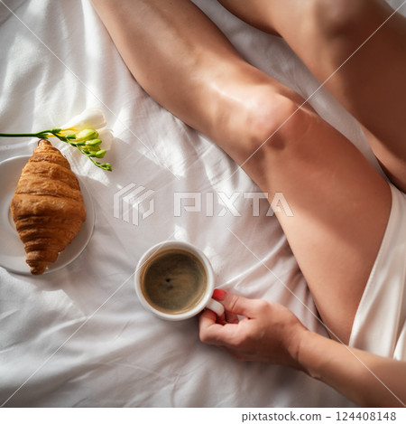 cropped shot of woman holding cup of coffee and croissant on bed cropped shot of woman holding cup of coffee and croissant on bed 124408148