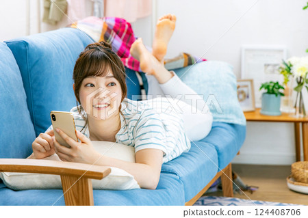 A woman operating a smartphone while relaxing on the sofa A woman operating a smartphone while relaxing on the sofa 124408706