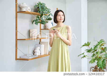 一位穿著夏裝的年輕女子在房間裡操作智慧型手機 124410317