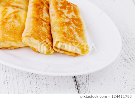 Thin pancakes with filling lying on white plate on wooden table 124411793