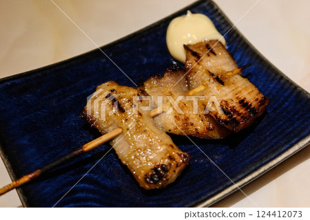 close up of Thai style grilled pork neck skewer with salad dressing on the side on a blue plate 124412073
