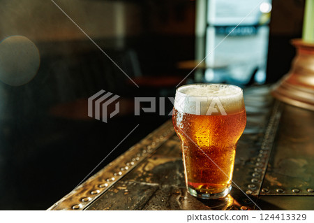 Craft golden beer in pint glass with condensation drops served on metal counter in daytime in vintage pub. Craft golden beer in pint glass with condensation drops served on metal counter in daytime in vintage pub. 124413329