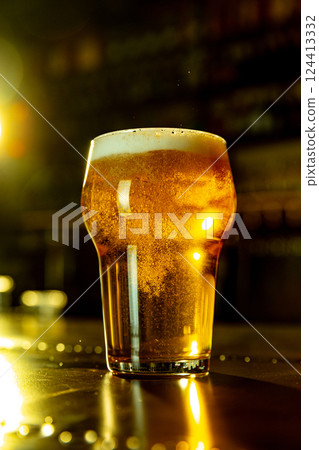 Close up photo of golden craft beer in pint glass with rich foam head glowing under warm bar lights. 124413332