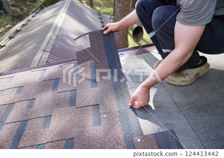 A close-up of the master's hands on the roof mounts flexible tiles. 124413442